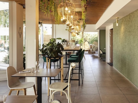 A dining area with a wooden ceiling, hanging lights, and potted plants.. Novotel Nancy