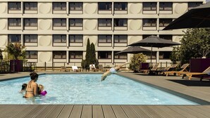 A swimming pool area with lounge chairs and umbrellas, a hotel building with a sign reading 'NOVOTEL' in the background. - Novotel Nancy (Laxou)