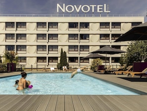 A swimming pool area with lounge chairs and umbrellas, a hotel building with a sign reading 'NOVOTEL' in the background. - Novotel Nancy (Laxou)