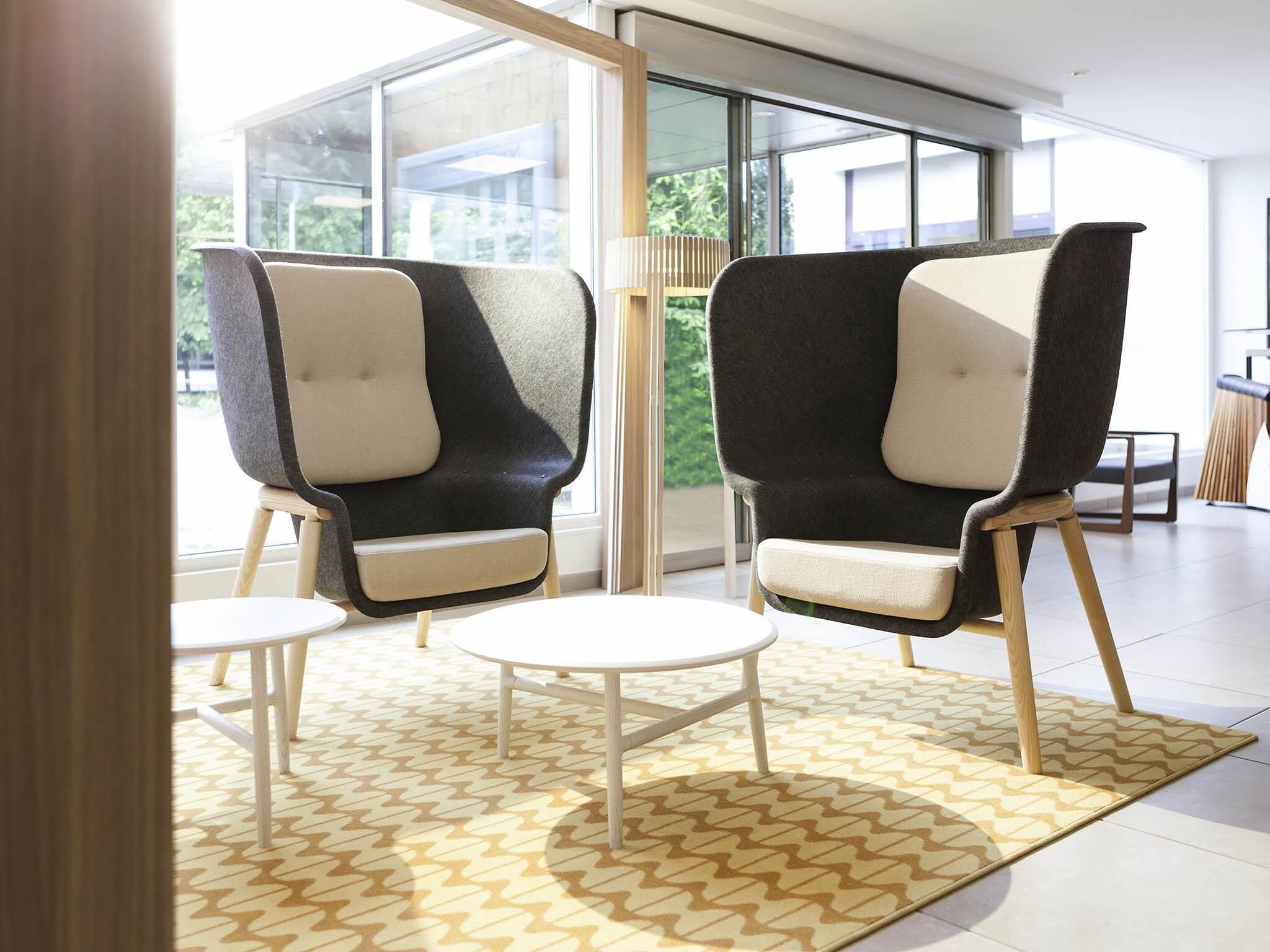 A modern interior with two armchairs and a small table, a patterned rug, and large windows offering a view of greenery.