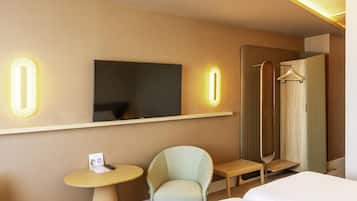 Camera d'albergo con un letto, una sedia, un tavolino, una TV e uno specchio con numeri illuminati.