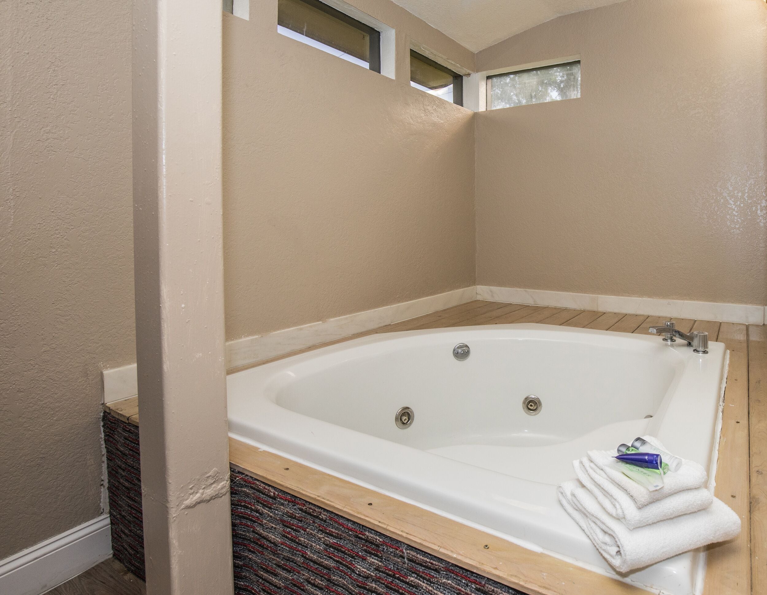 A large, white bathtub with a wooden base, a window above it, and a towel on the side.