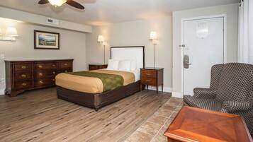 Habitación de hotel con cama, cómoda de madera, mesitas de noche, una silla y un ventilador de techo.