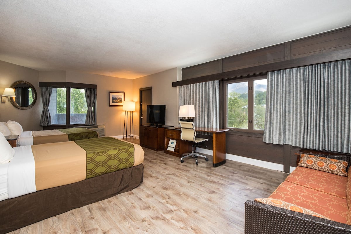 A hotel room with two beds, a desk, a chair, a television, and large windows with curtains.
