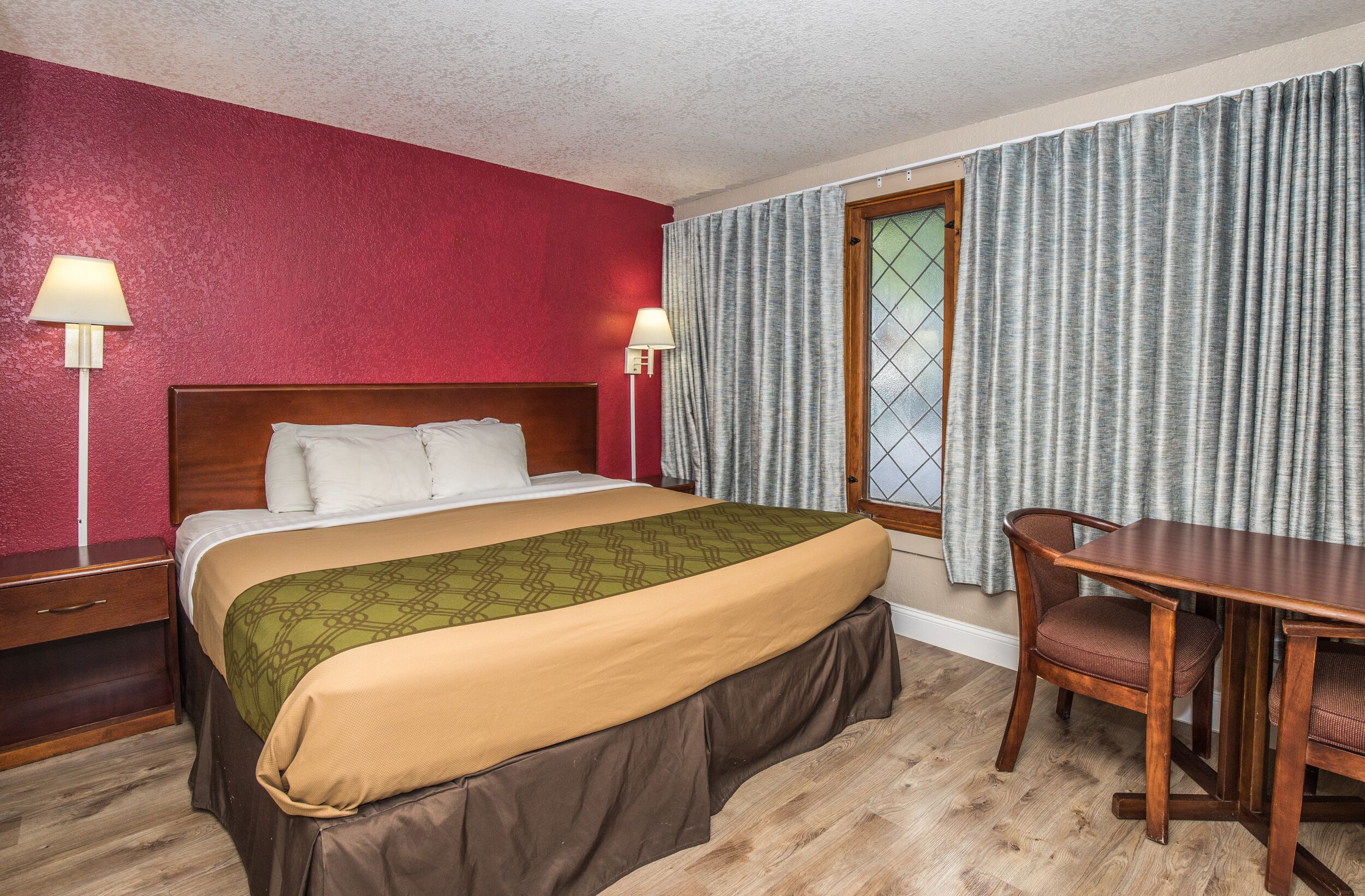 Quarto de hotel com cama, luminárias de cabeceira, uma mesa de madeira e uma cadeira.