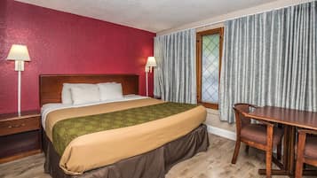 Quarto de hotel com cama, luminárias de cabeceira, uma mesa de madeira e uma cadeira.