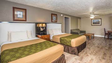 A hotel room with two beds, a nightstand with a lamp, a chair, a small table, and a ceiling fan.