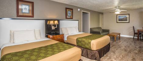A hotel room with two beds, a nightstand with a lamp, a chair, a small table, and a ceiling fan.