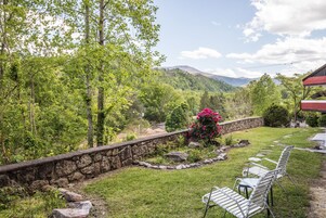 Un muro de piedra con jardín, un banco y vistas a montañas.
