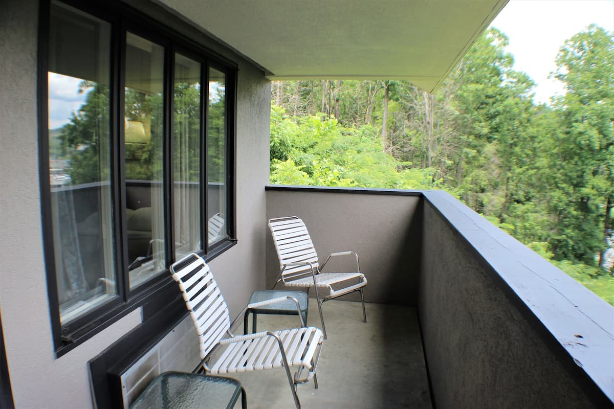 A balcony with two metal chairs and a table, overlooking a forested area.