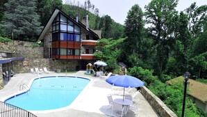 A pool area with lounge chairs and umbrellas, surrounded by a stone wall and lush greenery. - Chalet Inn (Gatlinburg)