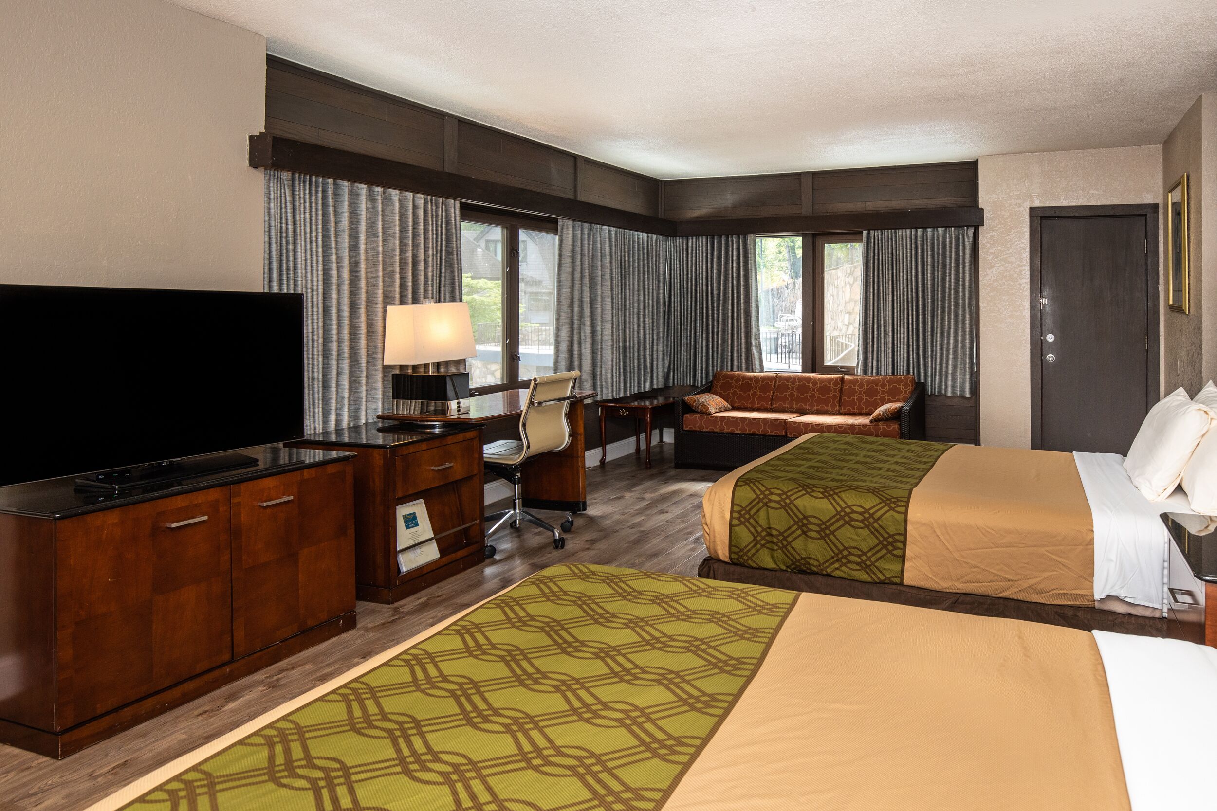 A hotel room with two beds, a desk with a chair, a television, and a lamp.