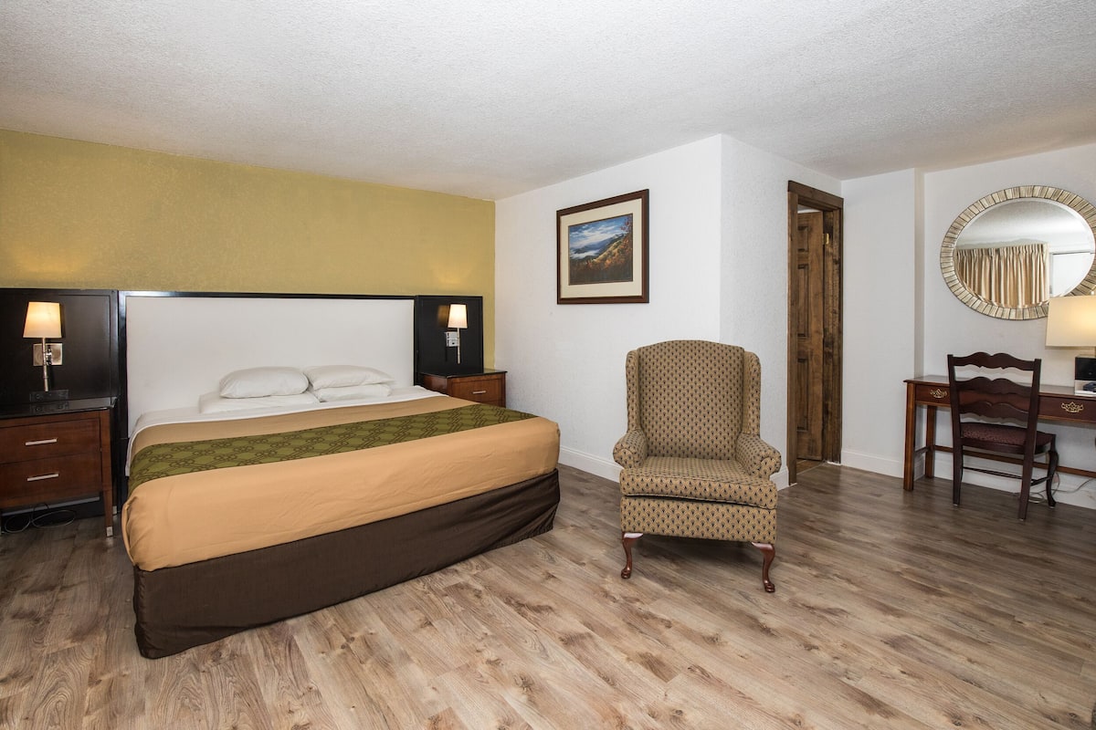 A hotel room with a large bed, a chair, a desk, and a mirror.