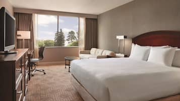 Une chambre d’hôtel avec un grand lit, un bureau avec une télévision, un canapé et une vue sur les arbres par la fenêtre.
