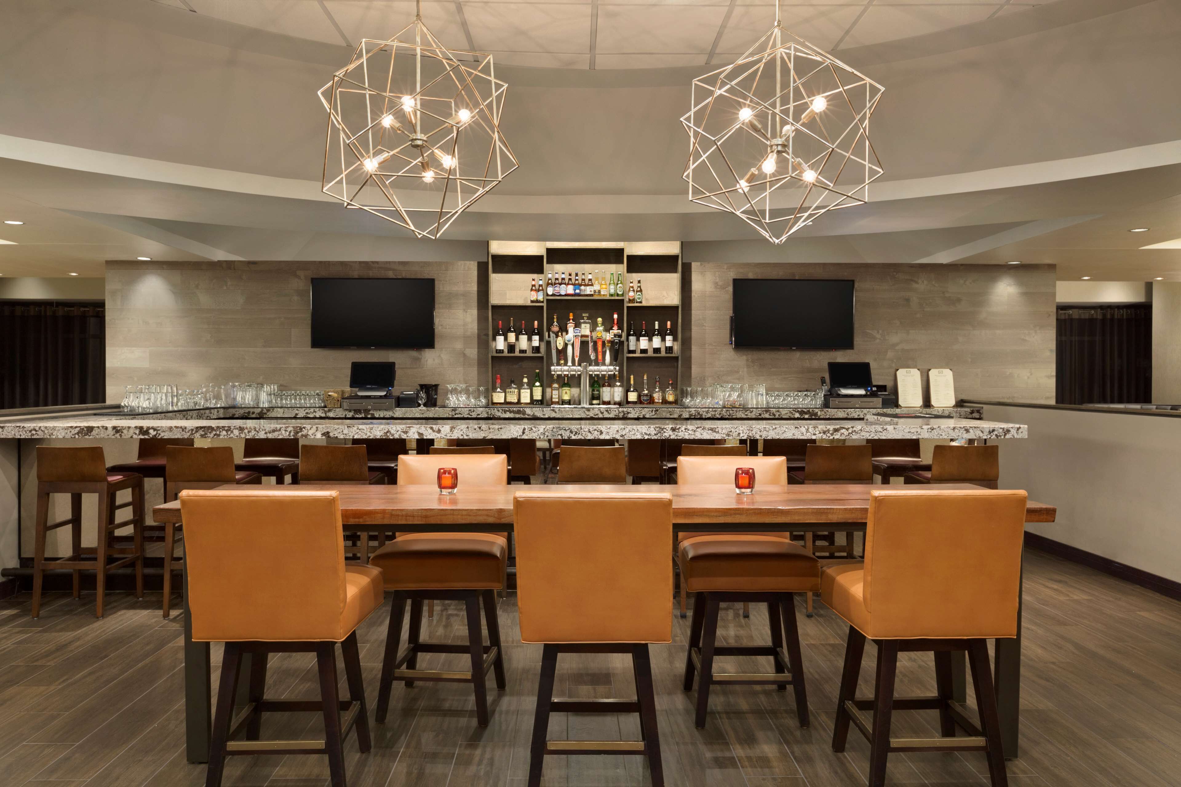 A bar area with a long counter, multiple bar stools, and a wine and liquor display.