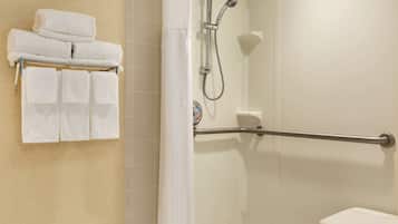 A bathroom with a shower, a toilet, and a towel rack with folded towels.