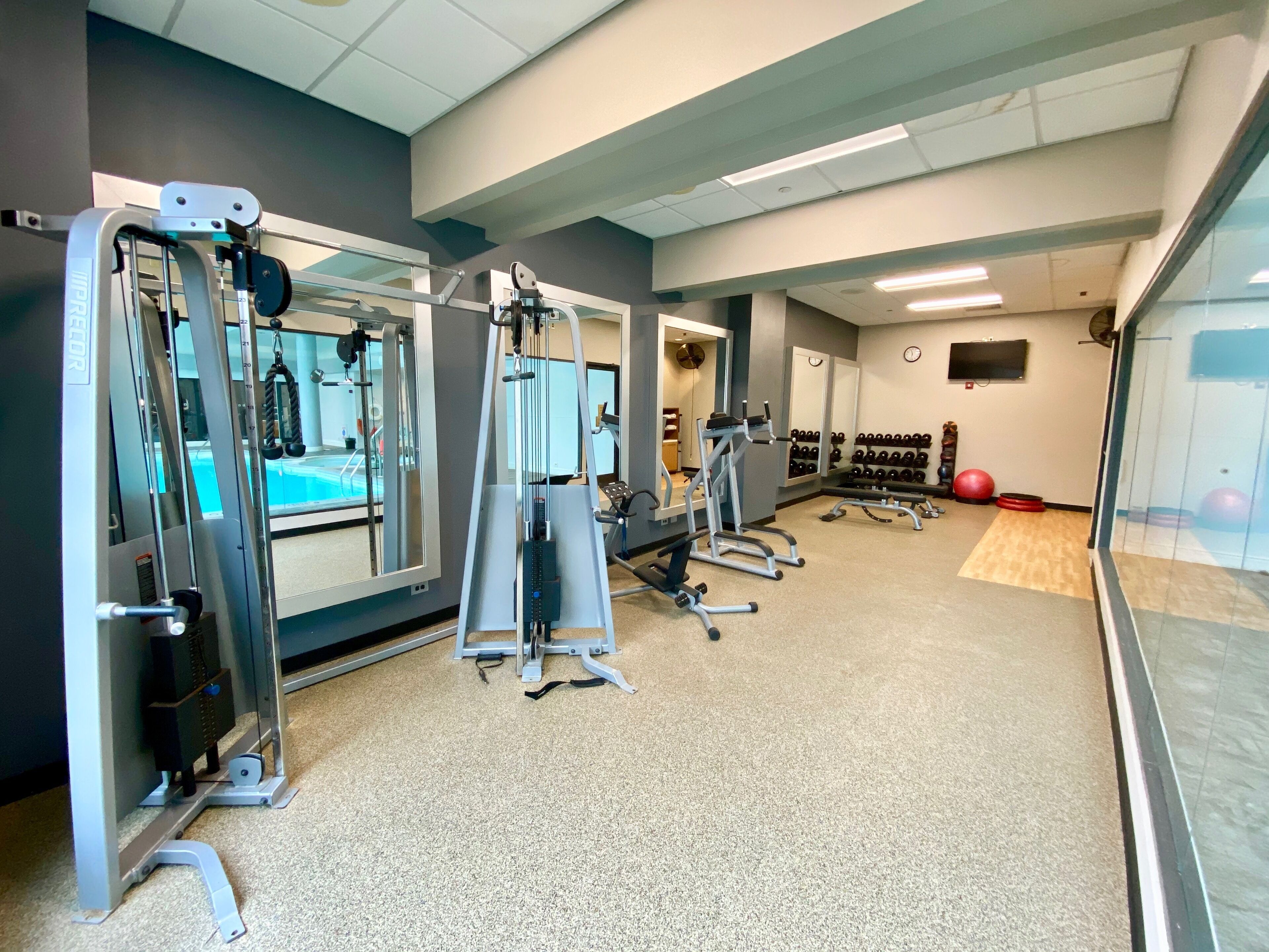 A gym with various exercise machines, a mirrored wall, and a wall-mounted TV.