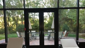A covered patio area with two lounge chairs, a table, and chairs, overlooking a garden with trees and a brick pathway. - Hilton East Brunswick Hotel & Executive Meeting Center (East Brunswick)