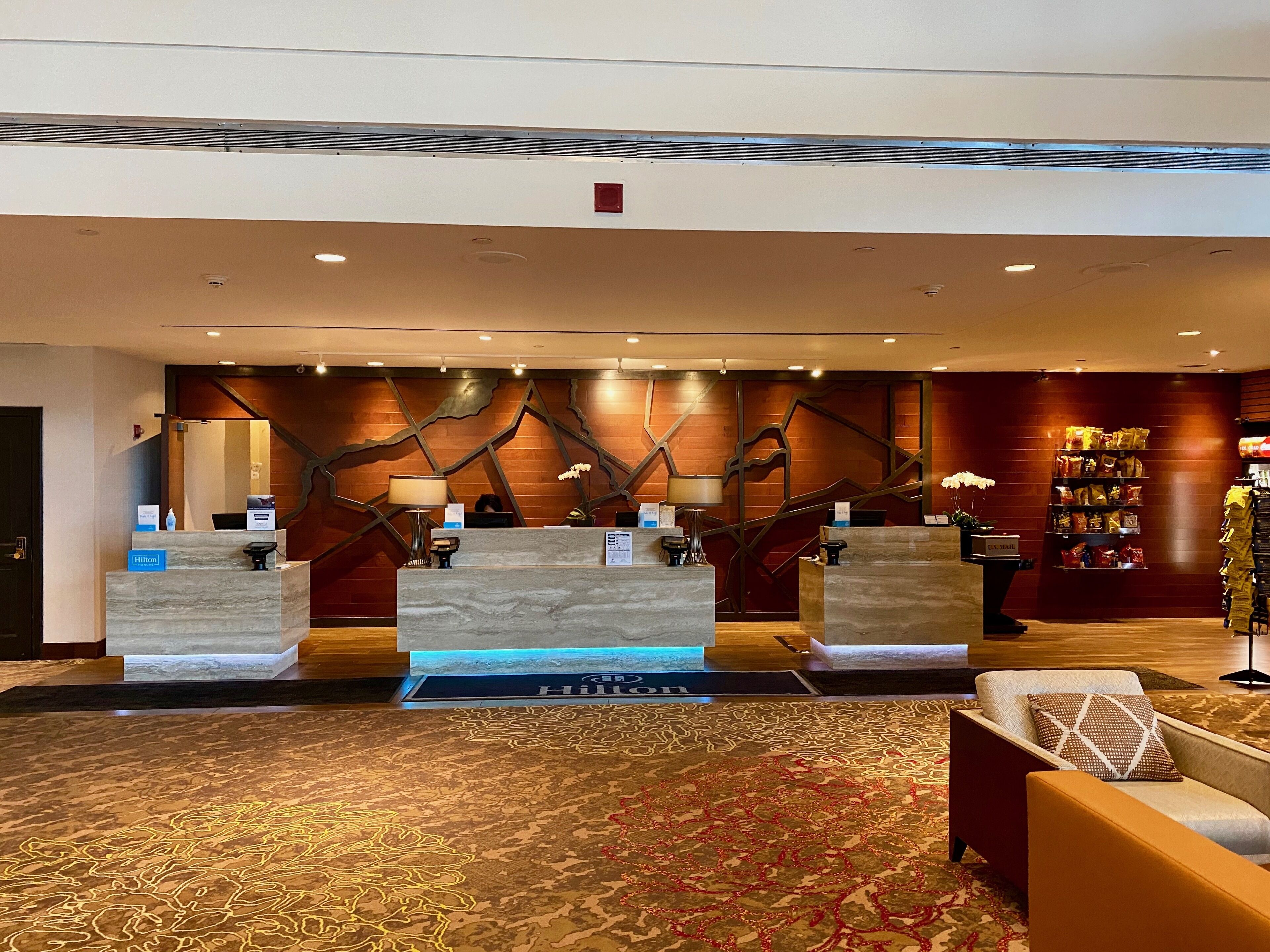A hotel reception area with marble counters, a reception desk, a red carpet, and a seating area with a patterned rug.