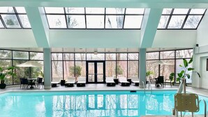 An indoor swimming pool with clear glass ceilings, lounge chairs, and potted plants. - Hilton East Brunswick Hotel & Executive Meeting Center (East Brunswick)