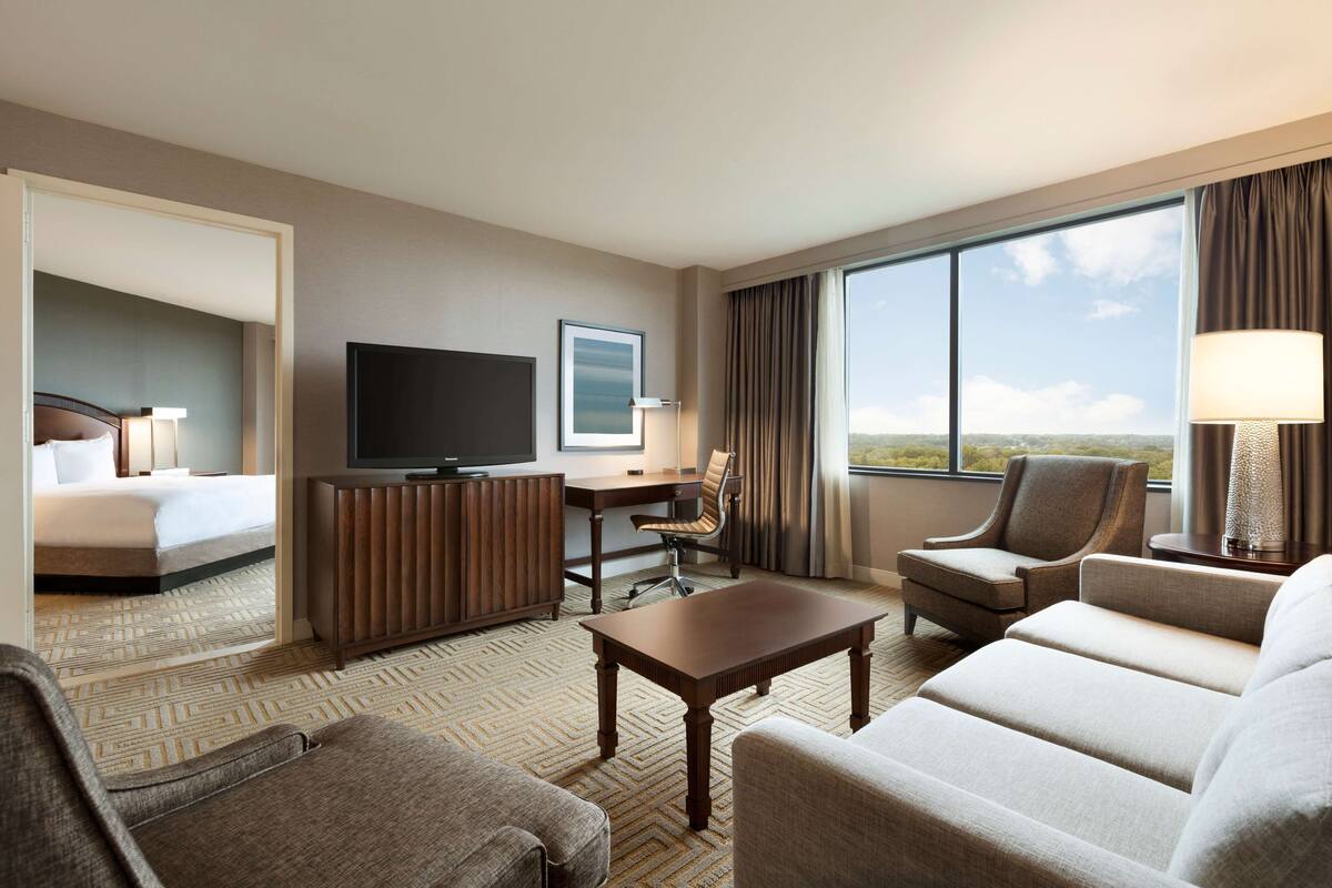 Ein Hotelzimmer mit Bett, Schreibtisch mit Stuhl, Fernseher, einer Sitzecke und einem großen Fenster mit Blick.