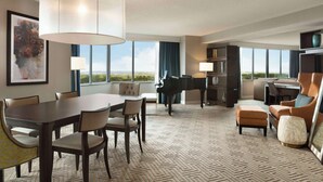 A spacious hotel room with a dining area, a piano, and a large window offering a view of the landscape. - Hilton East Brunswick Hotel & Executive Meeting Center (East Brunswick)