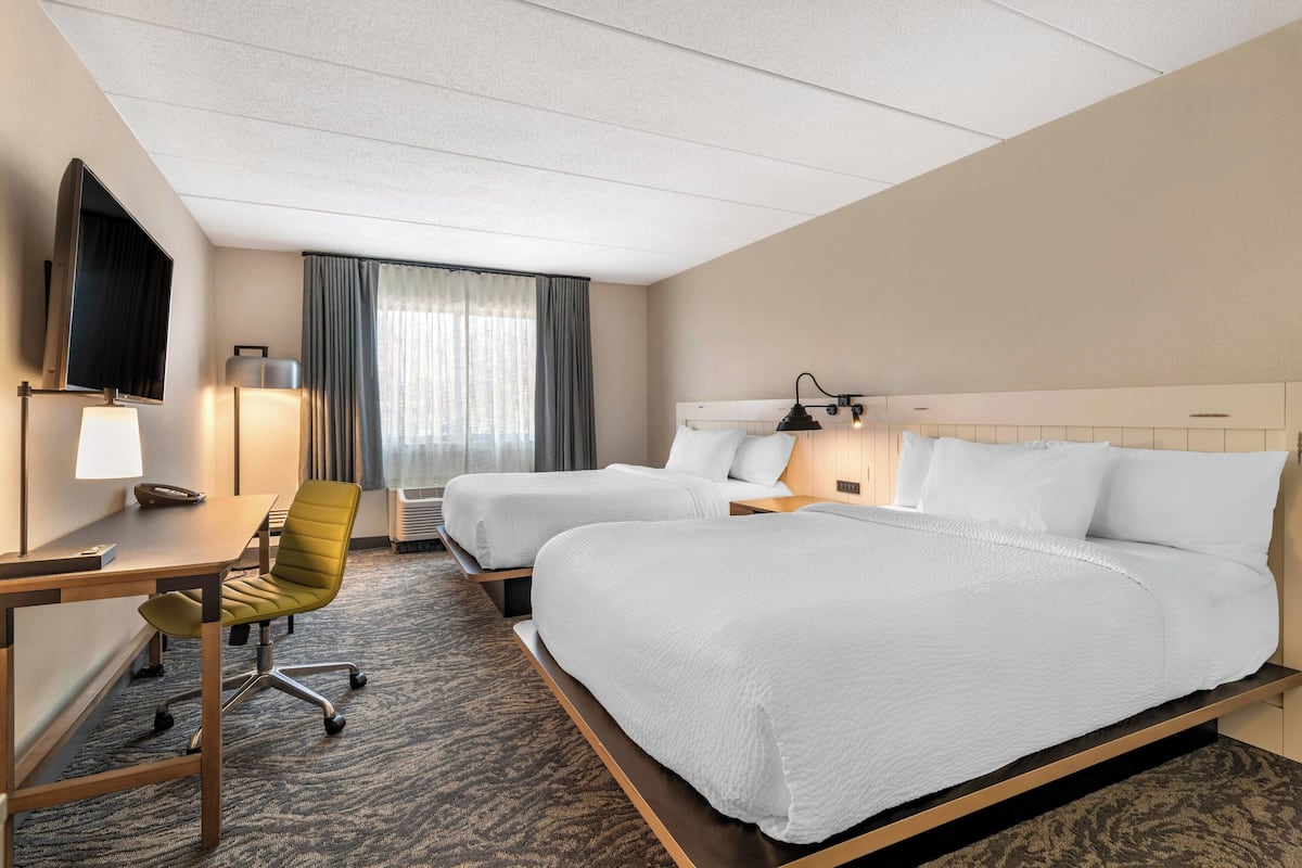 A hotel room with two beds, a desk, a chair, a TV, and a window with curtains.