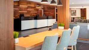 Un espace d’accueil moderne avec un comptoir de réception en bois, des sièges rembourrés de couleur grise et un éclairage suspendu.