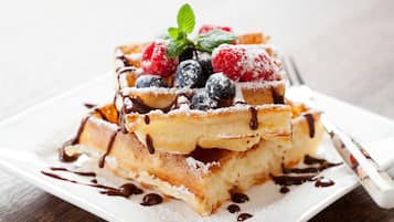 A stack of waffles with chocolate sauce and berries on a white plate.