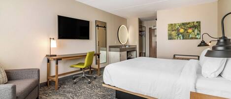 Ein Hotelzimmer mit Bett, Schreibtisch, Stuhl, Fernseher, Spiegel und einem Bild an der Wand.