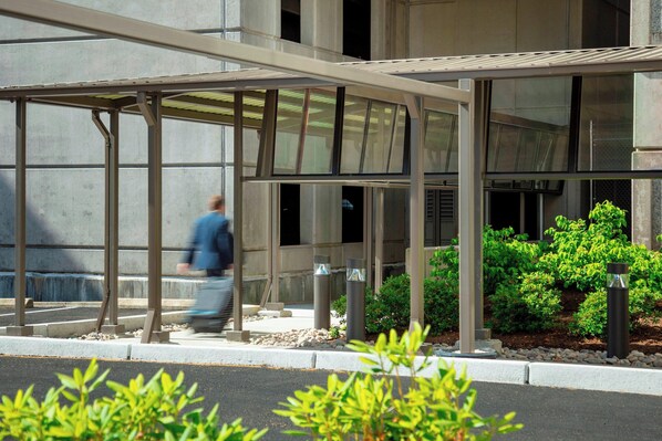 A modern building with a covered entrance area, a pedestrian pathway, and landscaped greenery.