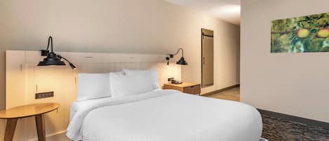 Een hotelkamer met een groot bed, twee nachtkastjes, een klein rond tafeltje, een spiegel en een schilderij aan de muur.