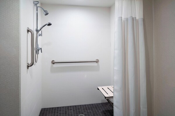 Un baño con ducha, barras de apoyo y un asiento.