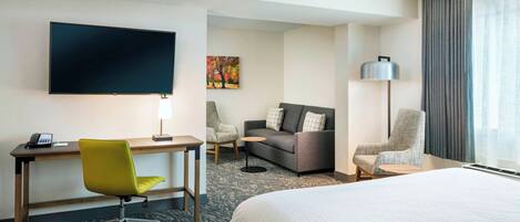 Habitación de hotel con cama, escritorio, silla, sofá, televisión y lámpara.