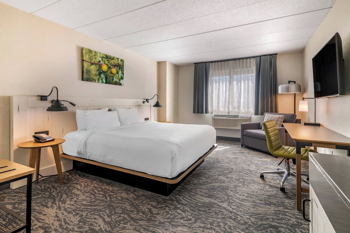 A hotel room with a bed, desk, chair, and a television.