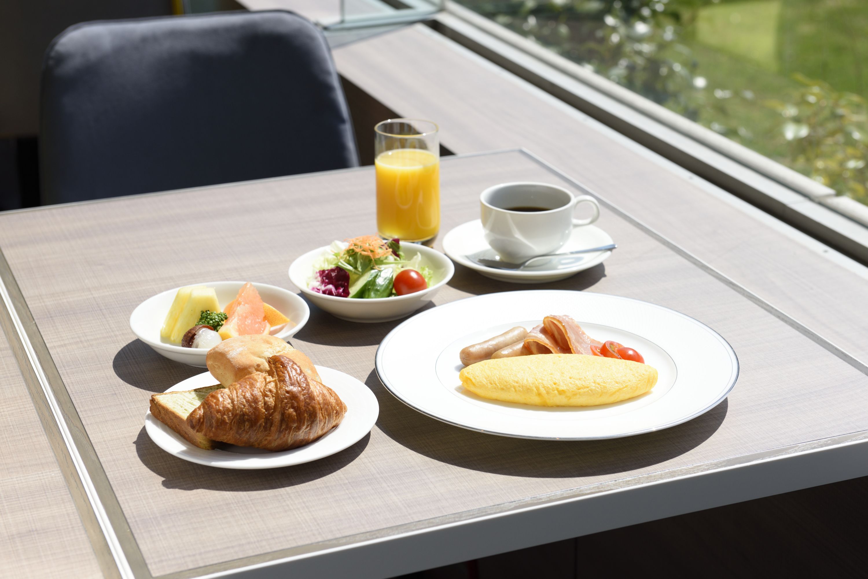 A breakfast table with croissants, an omelette, a fruit salad, a glass of orange juice, and a cup of coffee.