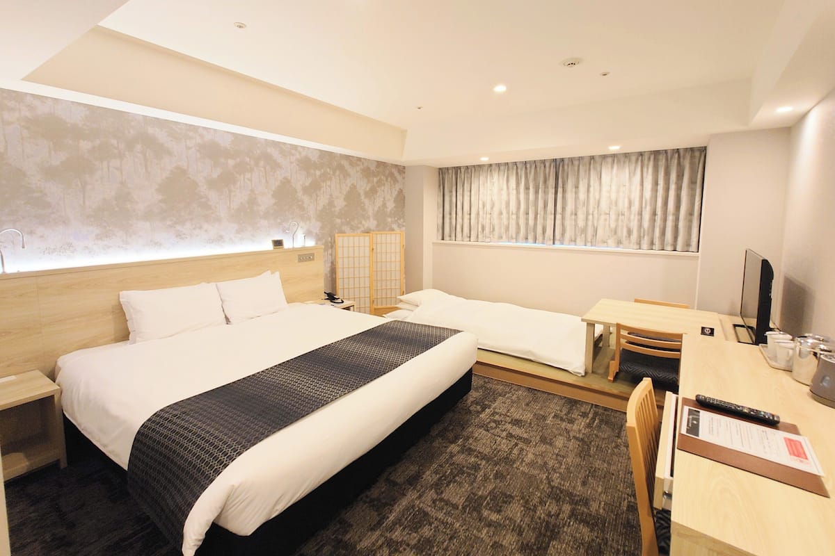 A hotel room with a large bed, a desk, a chair, and a TV.
