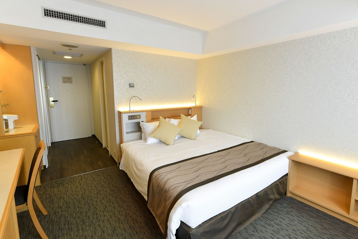 A hotel room with a bed, bedside table, and a desk with a chair.