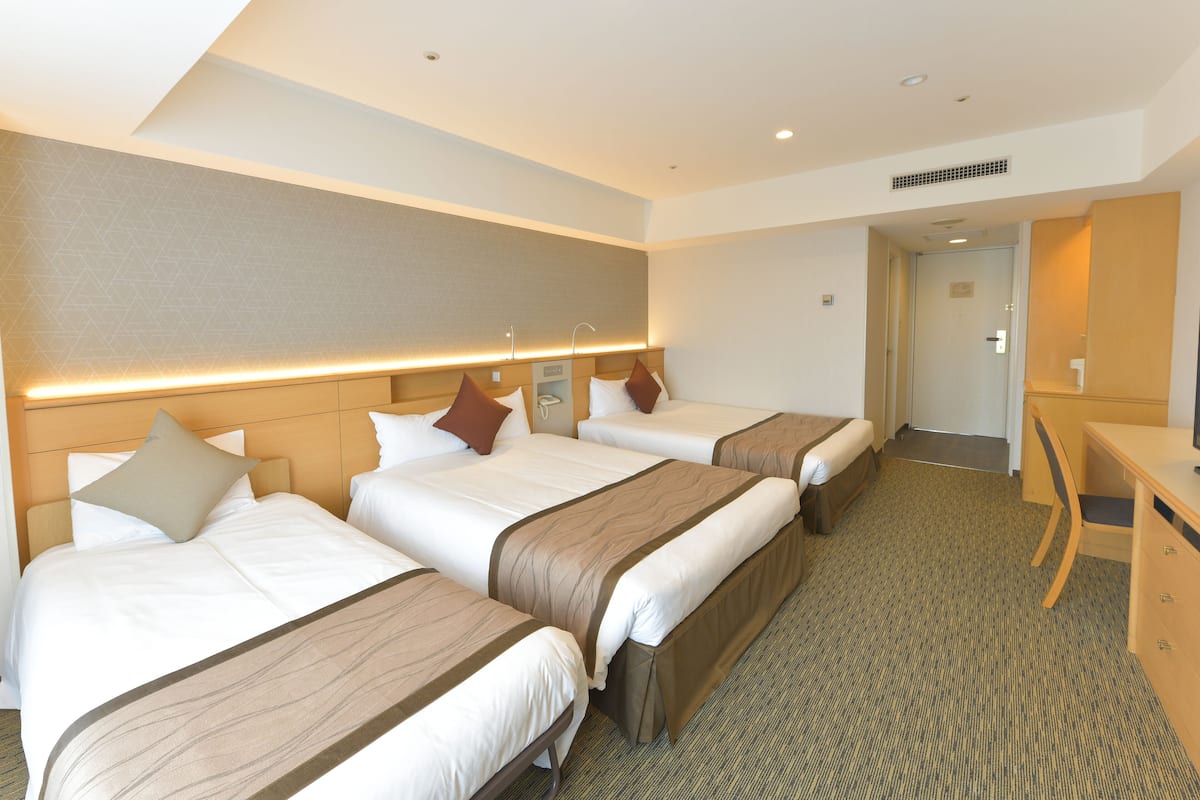 A hotel room with three beds, a desk, and a walk-in closet.