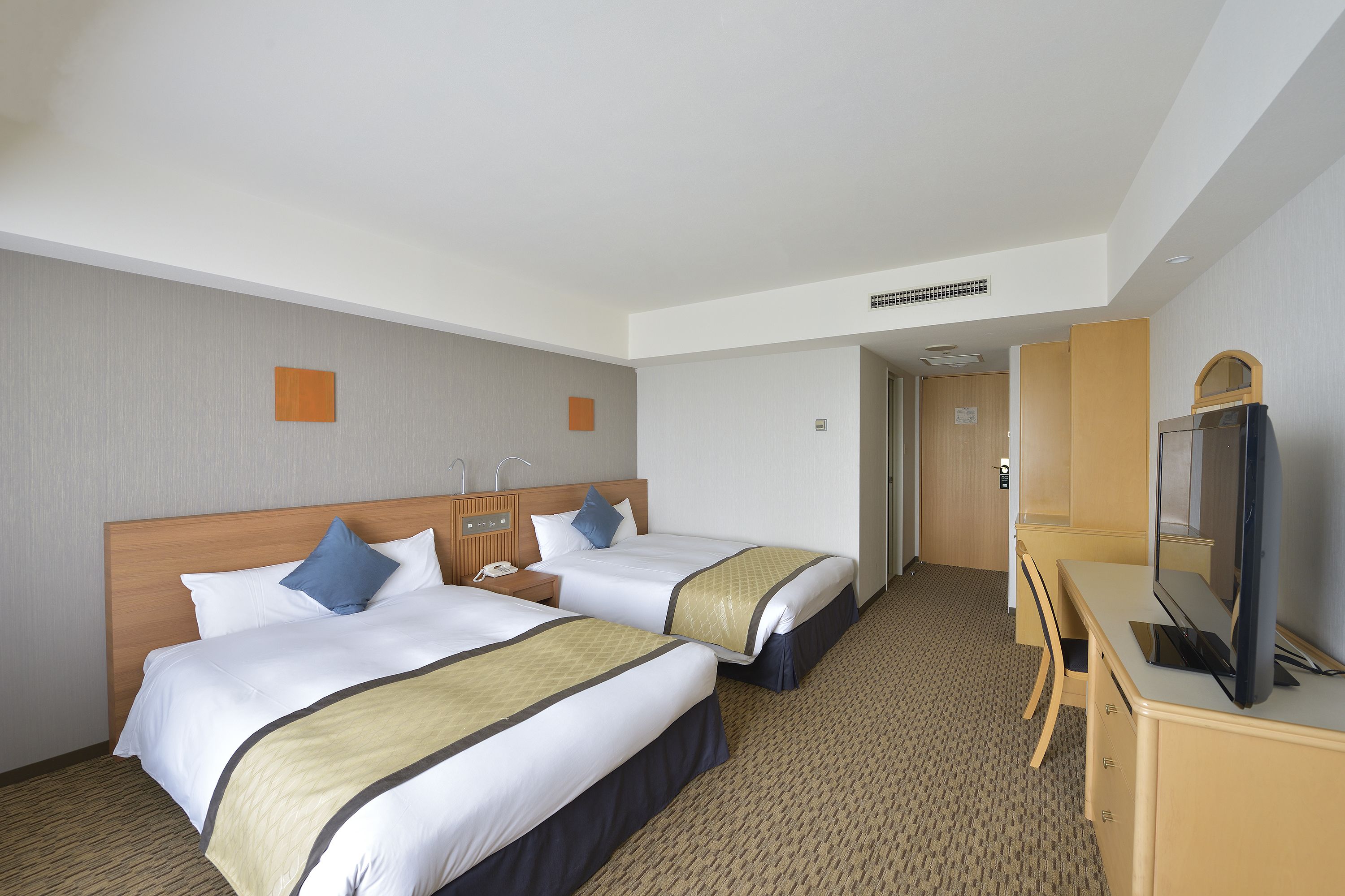 A hotel room with two beds, a desk with a TV, and a door leading to another room.