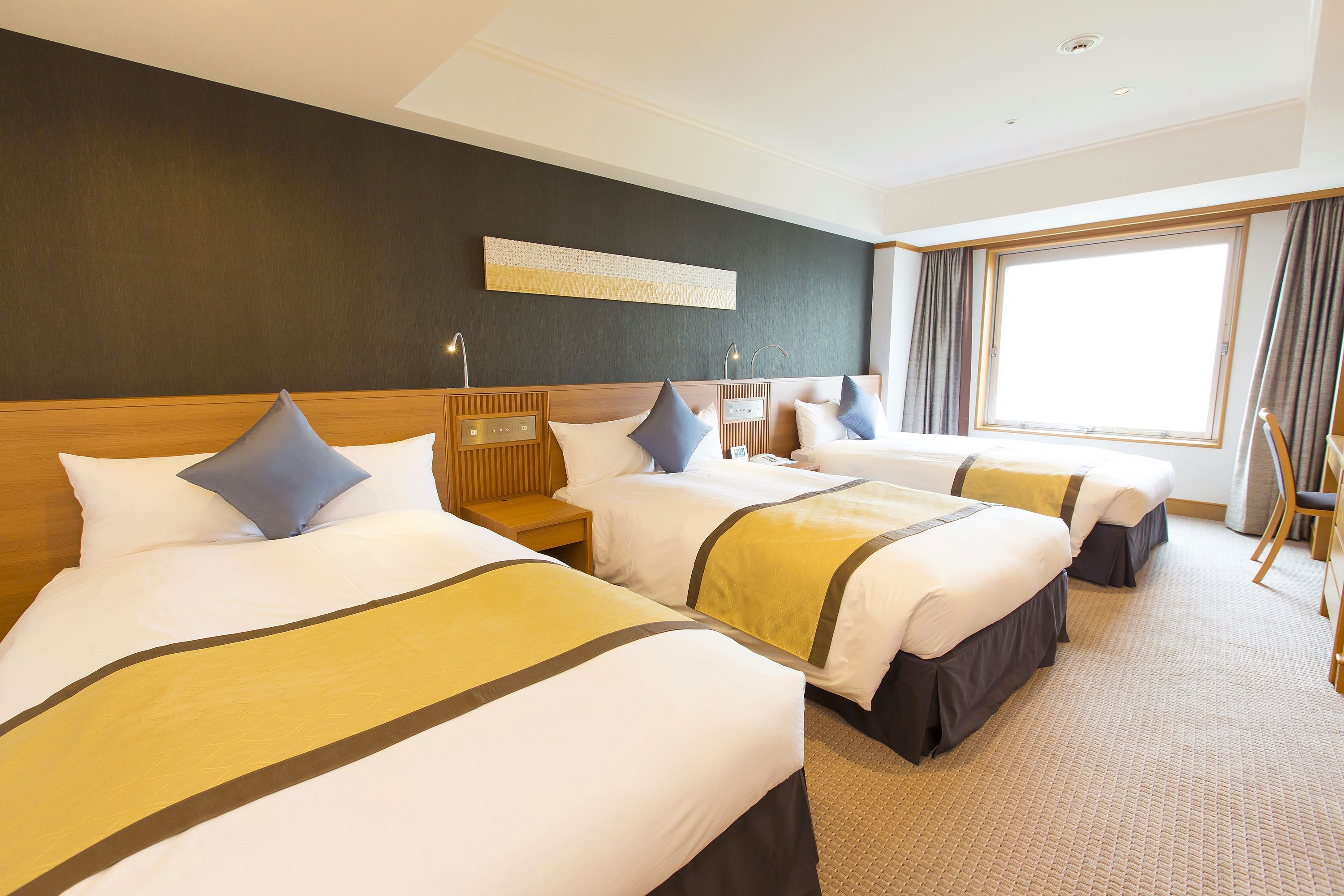 A hotel room with three beds, a large window, and a modern design.