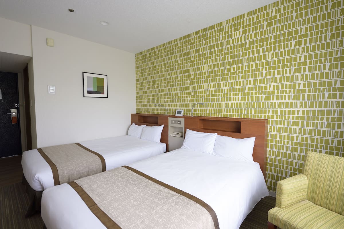 A hotel room with two beds, a wooden headboard, a chair, and a green mosaic wall.