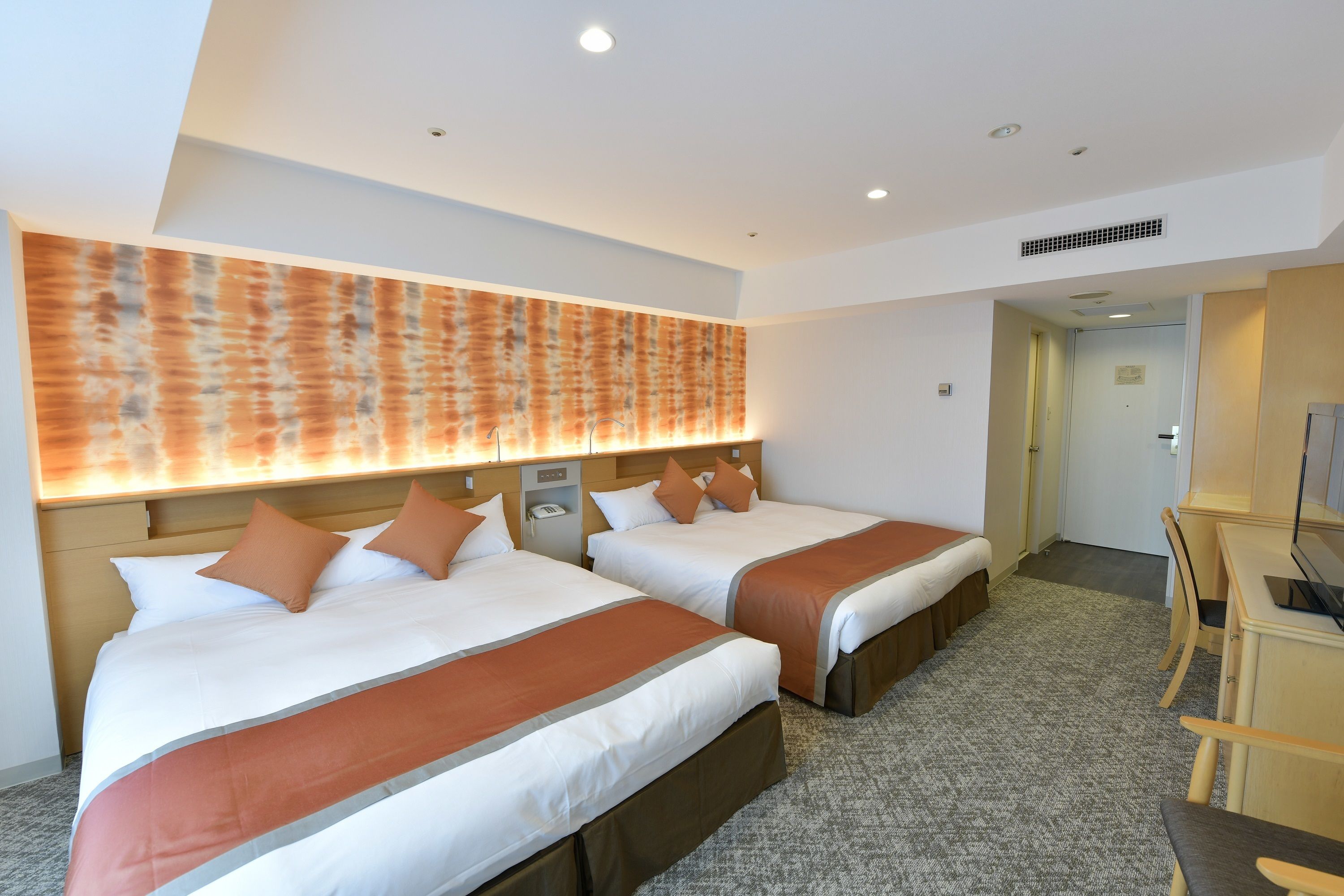 A hotel room with two beds, a desk, and a television.