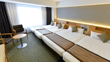 Habitación de hotel con dos camas individuales, un sofá, una mesita redonda y un ventanal con cortinas.