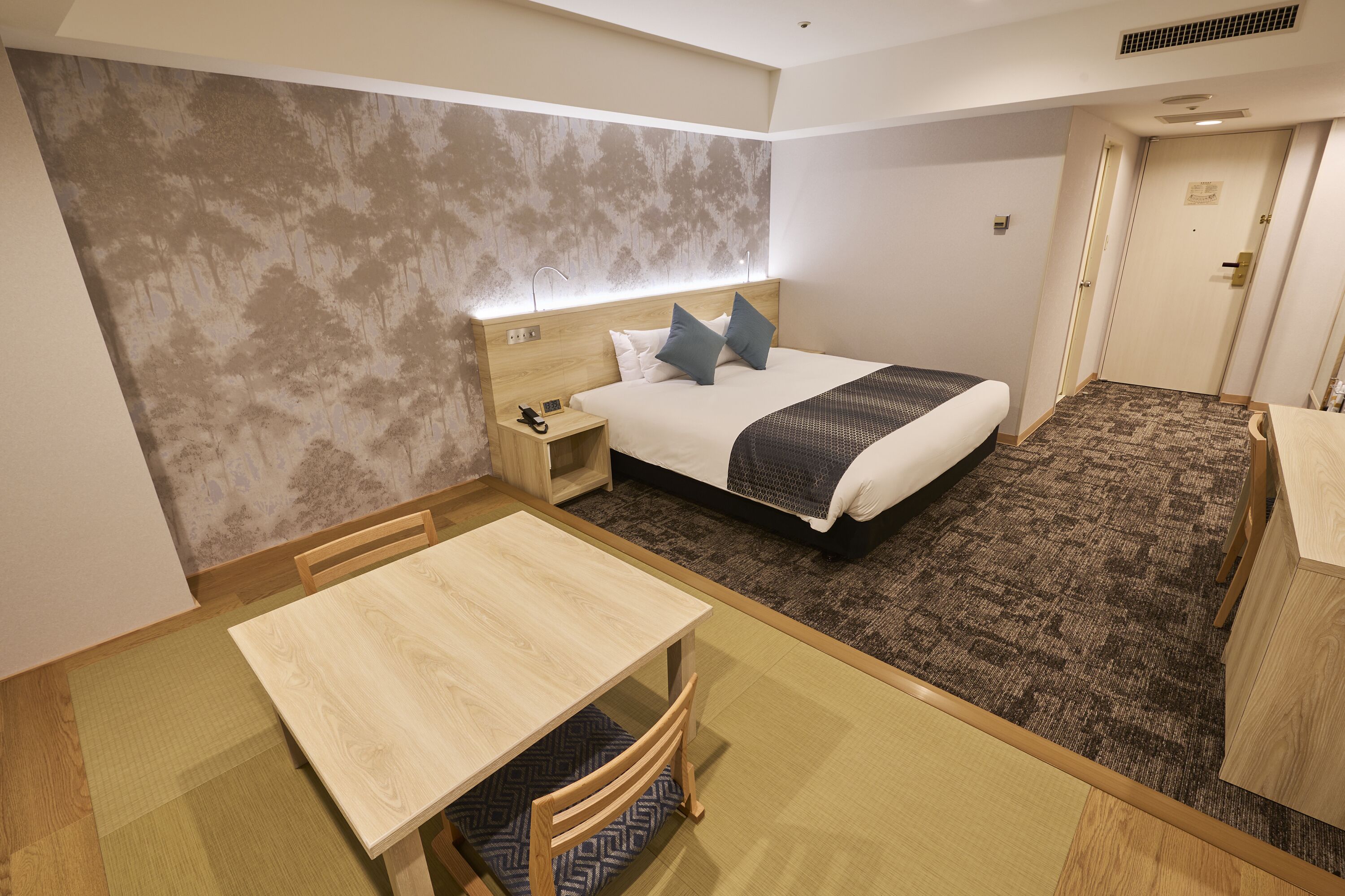 Hotellihuone, jossa on sänky, yöpöytä ja pieni pöytä tuoleineen.
