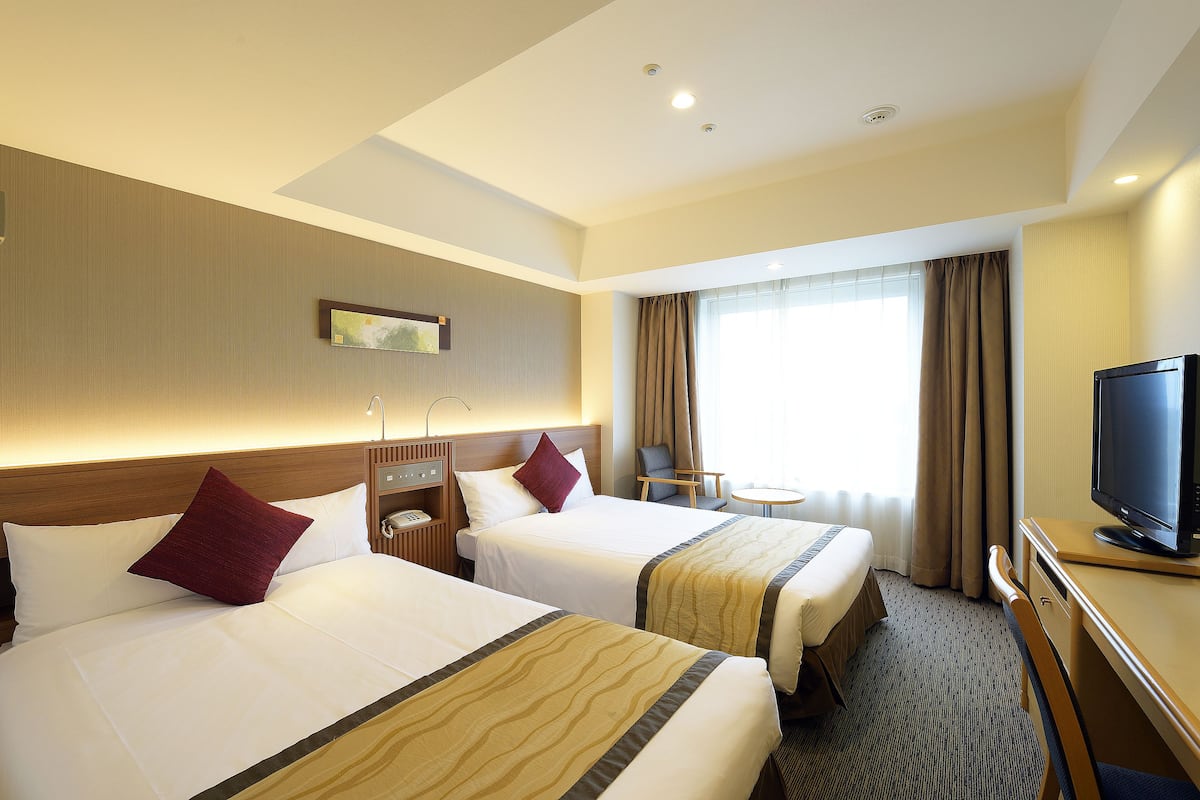 A hotel room with two beds, a desk with a television, a small table, and a chair.
