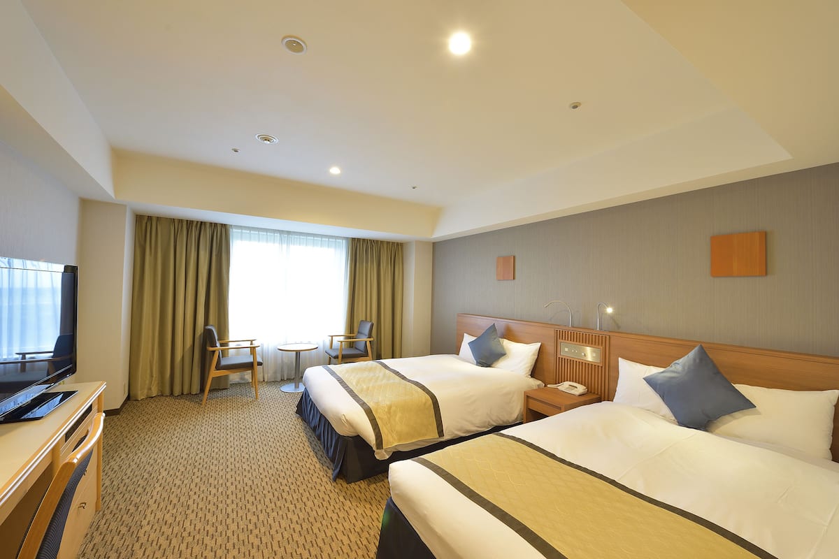 A hotel room with two beds, a desk with a computer, a chair, a small table, and a TV.