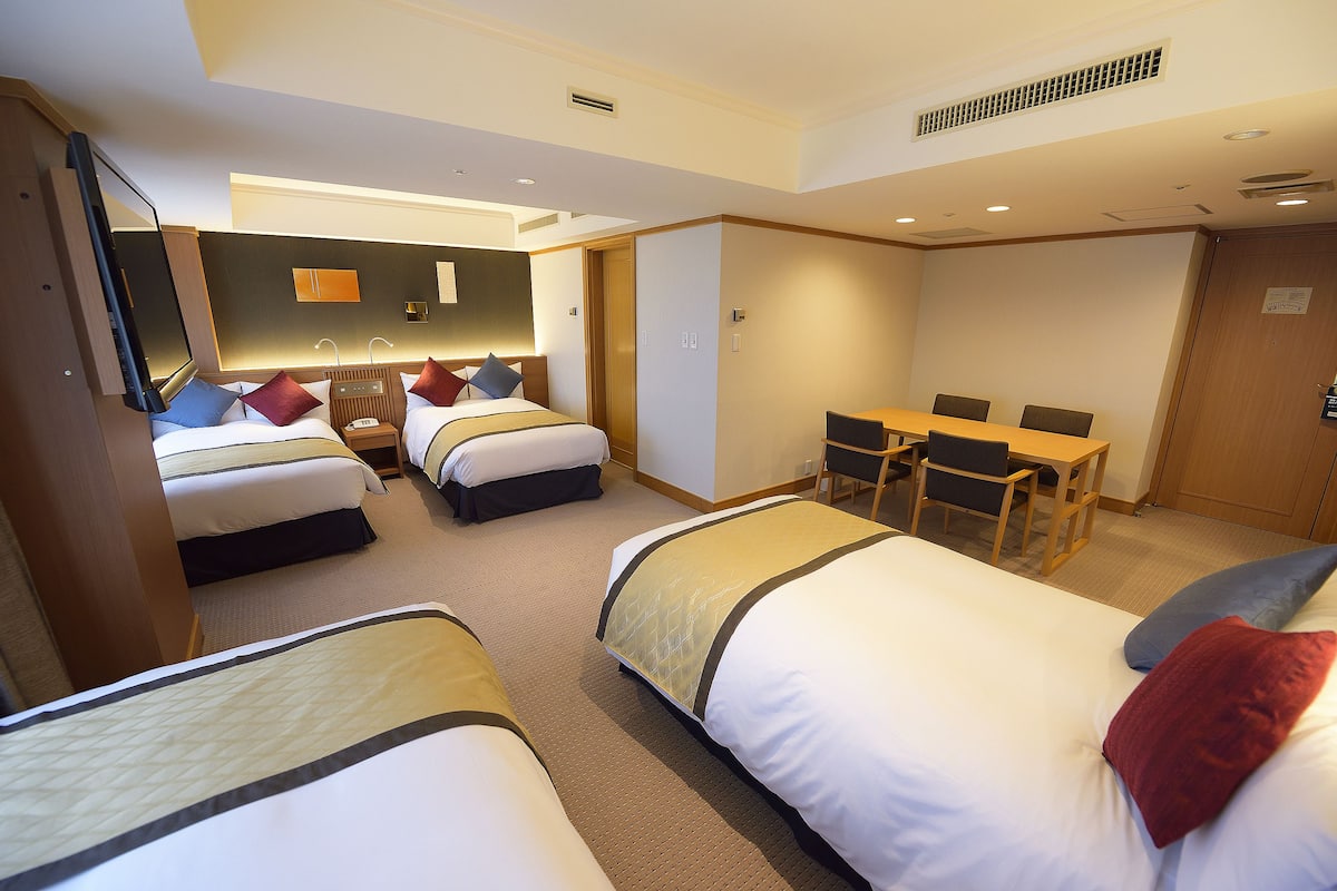 A hotel room with three beds, a desk, and a chair.