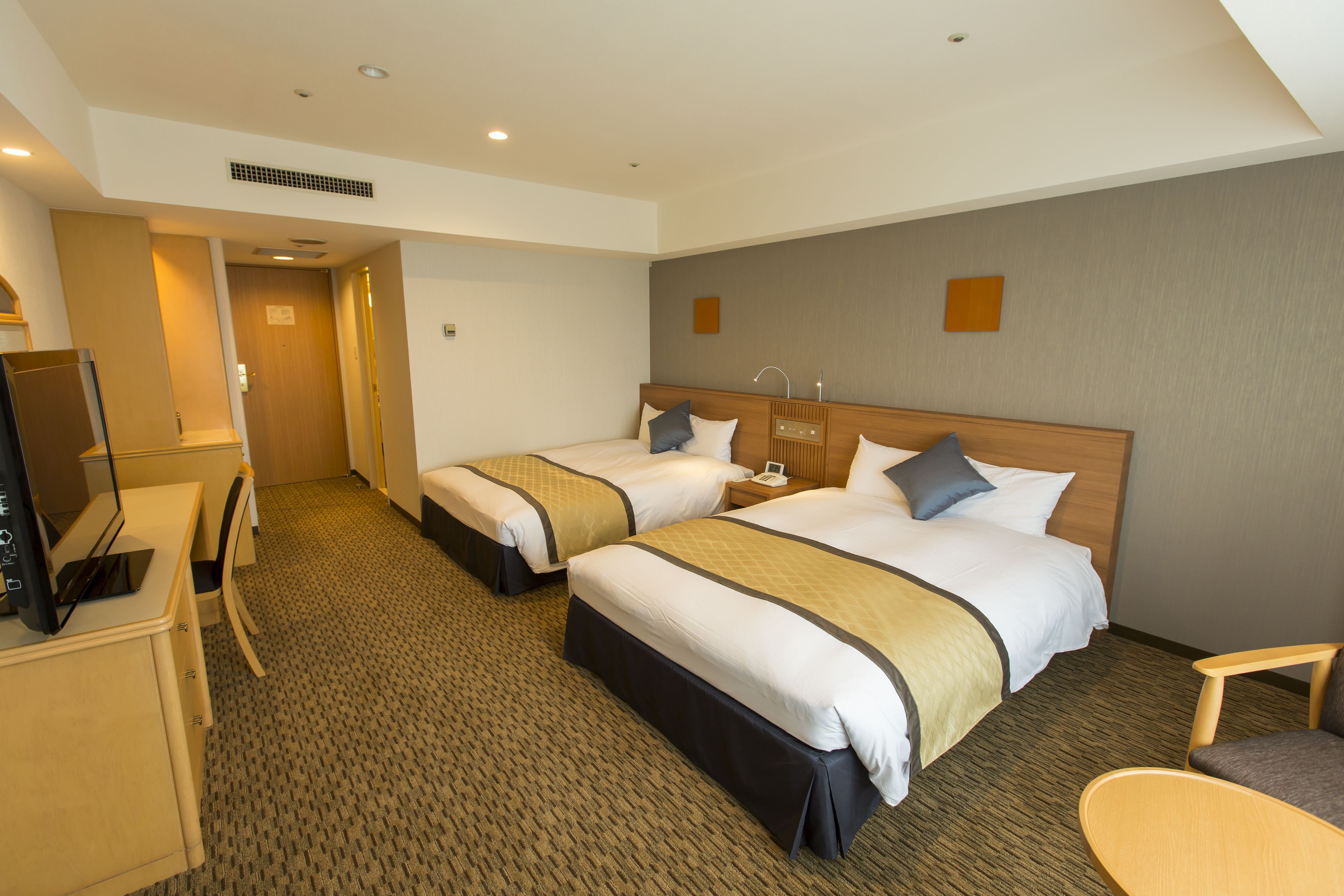 A hotel room with two beds, a desk, a chair, and a television.