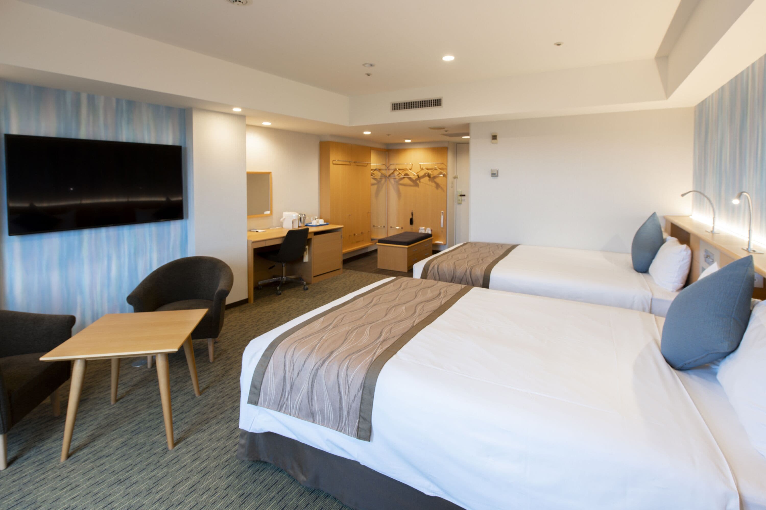 A hotel room with two beds, a desk, a chair, a TV, and a wardrobe.